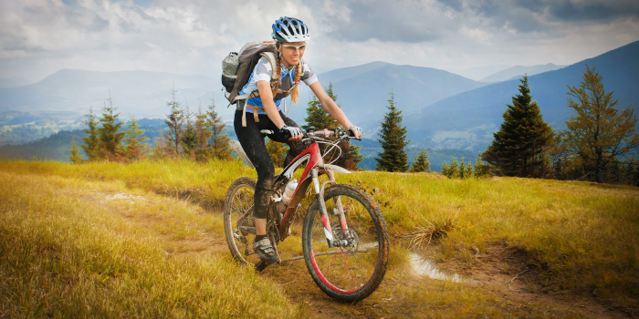 A woman rides down a wilderness track with hills in the background